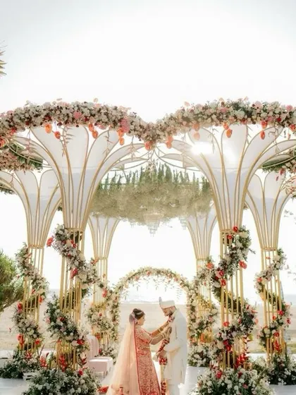 A magnificent mandap structure with a mirrored ceiling reflecting the couple and the sky, framed by spiraling floral arrangements.