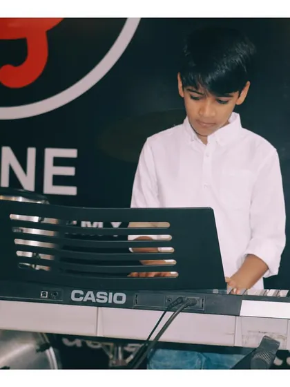 A young keyboard student practicing during a class. You can see his focus as he works on a piece, with the drums visible in the background, showing our multi-instrument environment.