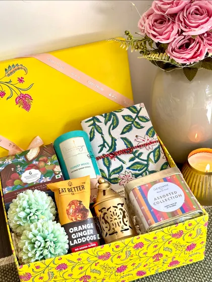 A bright and sunny yellow Diwali box, containing a handcrafted diary, a lamp, Goodwyn tea bags, and dhoop sticks.