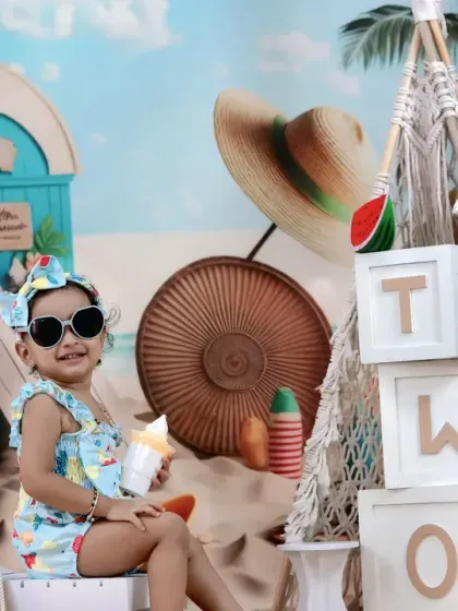A baby girl celebrates turning two with a fun beach party theme, complete with sunglasses and a big smile.
