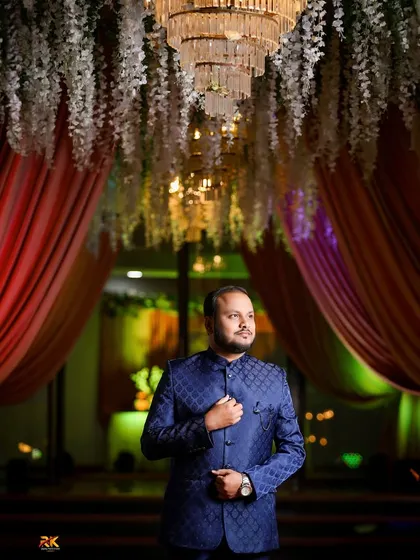 A powerful, low-angle shot of the groom in his royal blue Jodhpuri suit. The grand decor of the reception hall frames him perfectly, creating a sense of occasion.