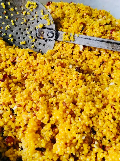 A large batch of Boondi, small fried gram flour balls, ready to be made into ladoos or added to other dishes. The texture is light and crispy, a result of careful preparation.