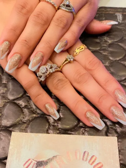 Long, coffin-shaped nails with a unique design. A sheer white base is topped with a geometric pattern filled with sparkling gold glitter.