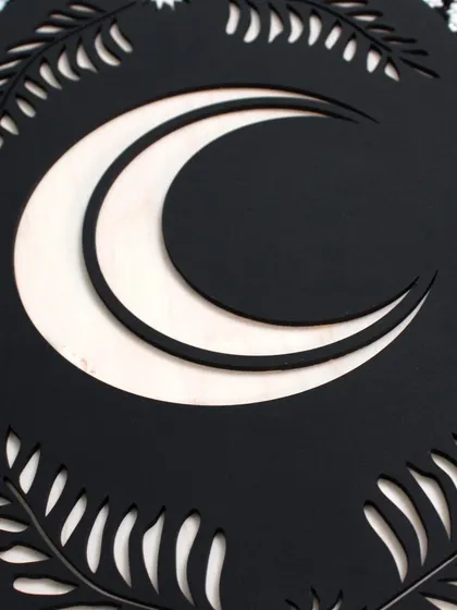 A detailed shot of the crescent moon and surrounding leaves, showcasing the contrast between the black background and the natural light wood finish.