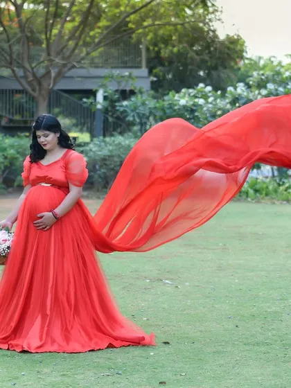 A beautiful, dynamic shot of a mom-to-be in a red gown with a long, flowing train, captured mid-air in a green park.