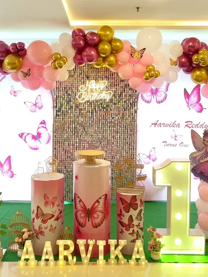 A butterfly-themed first birthday with a pink and gold color scheme. The setup includes a large marquee number '1' and a cute fairy cutout.
