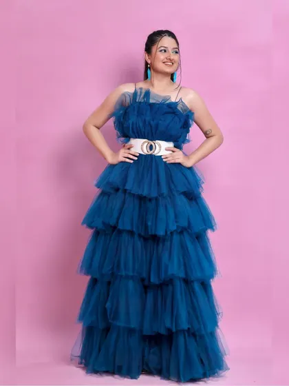 Our peacock blue ruffle gown is a showstopper. Here it is styled with a wide white belt against a solid pink backdrop for a bold color contrast.