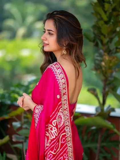 An outdoor portrait of Ashika Ranganath in a beautiful pink saree. The natural greenery in the background adds a fresh, vibrant feel to this classic look.