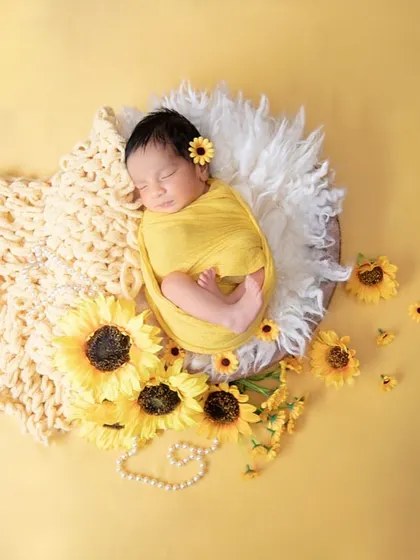 A peaceful newborn wrapped in sunny yellow, nestled among sunflowers on a soft, fluffy surface. This image radiates warmth, happiness, and the joy of a new beginning.