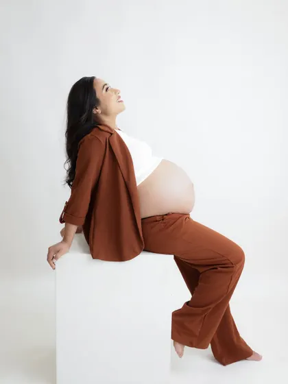 A joyful and confident portrait. The mom-to-be is seated in a stylish brown suit, her happy expression lighting up the frame.