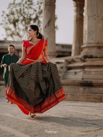 A bride-to-be walks with grace through a pillared corridor, her traditional half-saree adding a splash of color to the ancient architecture.