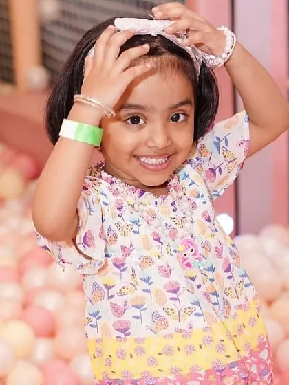 A happy girl poses for the camera, surrounded by a sea of pink and white balls.
