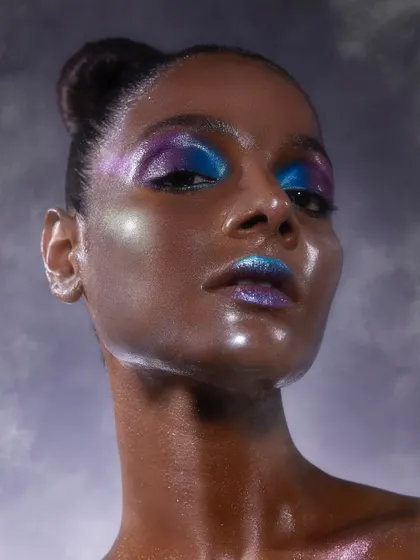 A futuristic glass skin look with a duo-chrome blend of blue and purple on the eyes and lips. This shows the high level of creativity our students achieve.