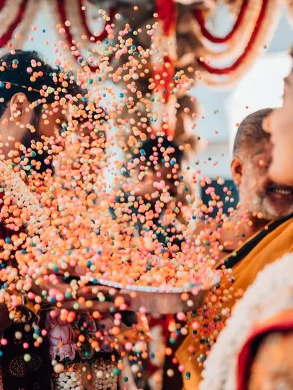 A candid shot of the bride's reaction as the groom showers her with colorful puffed rice during a fun wedding ritual.