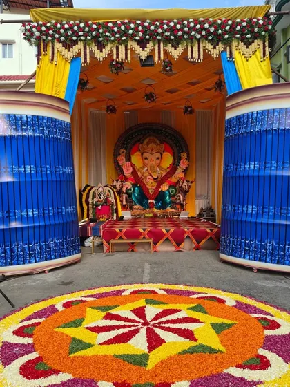 This is a large-scale outdoor pandal we constructed for a Ganesh Chaturthi festival celebration. The setup includes a decorated stage for the idol, vibrant yellow and blue fabric draping, and a massive, colorful flower rangoli on the ground, perfect for community and corporate festive events.