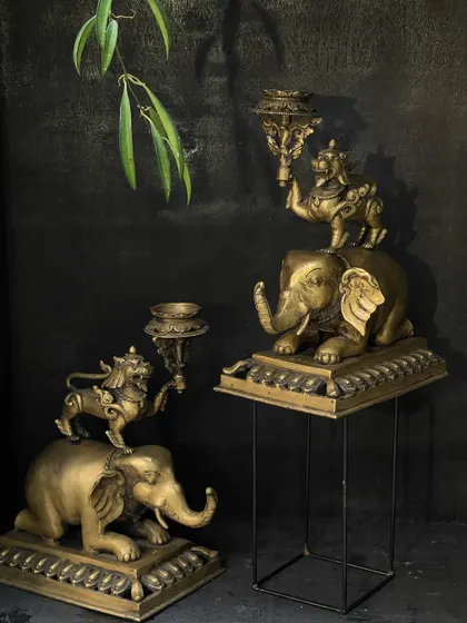 A pair of Tibetan-style brass candle stands, featuring a lion on top of an elephant. This vintage, beautifully crafted pair will add a unique Asian charm and warm candlelight to any space.