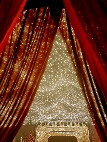 A glimpse of the grand entrance through parted red velvet curtains, revealing the ceiling of twinkling fairy lights within. This creates a sense of theatricality and excitement.