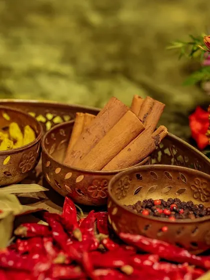 A close-up of the tray of auspicious spices, including turmeric, cinnamon, peppercorns, and red chillies. This detail is an ode to purity, good omens, and the sensory richness of Indian traditions.