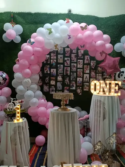 A pink and white balloon arch over a photo collage backdrop, creating a personalized centerpiece for a first birthday.