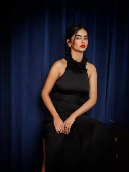A powerful portrait in a black ensemble with a ruffled high-neck top. The bold red lip and the deep blue background create a classic, dramatic look.