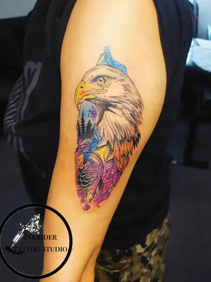 This colorful eagle tattoo on the upper arm combines realism with abstract watercolor effects. This style is perfect for covering larger areas or complex old tattoos with a vibrant and artistic piece.