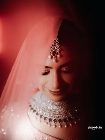 A close-up bridal portrait focusing on the bride's serene expression and intricate diamond jewelry, captured with soft, dramatic lighting.