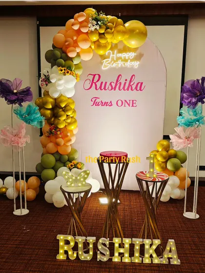 A simple yet sweet first birthday setup for Rushika. The decor features a minimal backdrop with a colorful balloon garland and light-up letters, perfect for a smaller, intimate celebration.