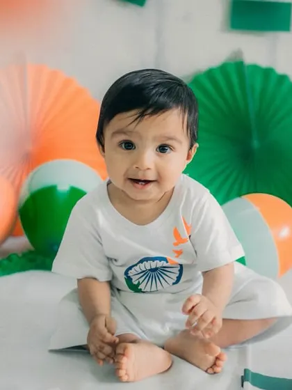 A sweet smile and direct eye contact make this a heartwarming portrait. The baby is sitting comfortably among the orange, white, and green decorations.