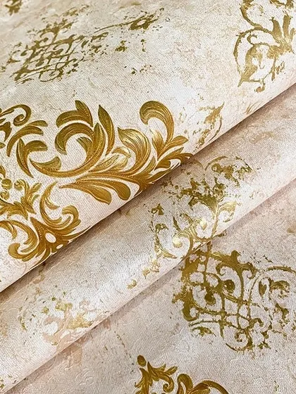A close-up of a cream-colored wallpaper with a distressed look and a classic gold damask pattern.