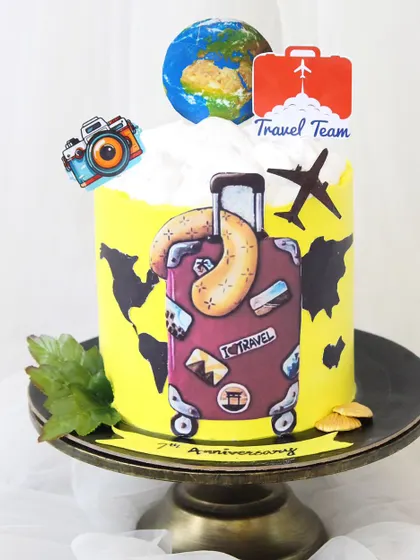 This travel-themed cake was created to celebrate a 7th anniversary for a travel company. It features a bright yellow world map base, a fondant suitcase, and other travel icons like a camera and airplane.