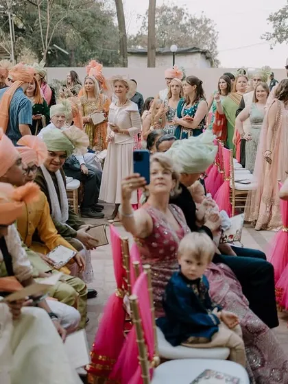 A candid shot of the wedding guests. Everyone is engaged in their own little moments, from taking selfies to watching the kids, creating a rich tapestry of the day.