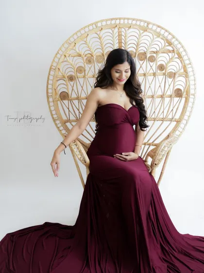 A classic and elegant portrait on a wicker peacock throne. The rich burgundy gown and serene pose create a timeless and regal image.