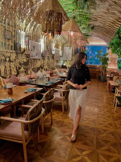 A candid shot in a stylish restaurant, wearing a chic black top and white skirt, perfect for lifestyle or influencer-style campaigns.