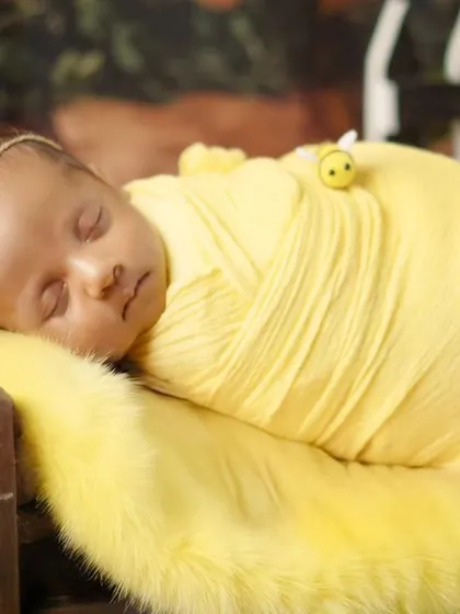 A side profile of the sleeping newborn in the honeybee theme. This angle highlights the baby's delicate features against the soft yellow fur.