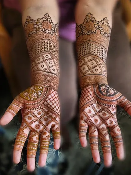 A beautiful example of geometric and floral fusion in bridal mehndi. The palms are covered in intricate check patterns, while the arms feature softer, more traditional motifs.