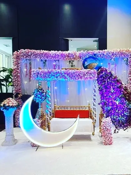 An elegant baby shower decoration with a white carpet, a peacock made of purple flowers, and a lighted moon prop, creating a luxurious feel.