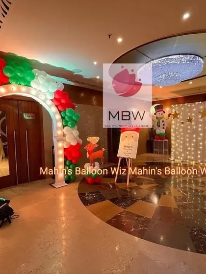 The entrance to the Christmas party, featuring a light-up arch with red and green balloons and a welcome sign with a snowman prop.