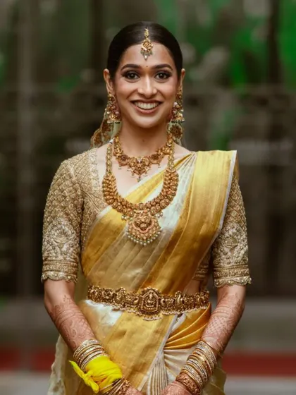 A smiling bride in her golden-yellow Kanchipuram saree and heavily embroidered blouse. This classic South Indian bridal look is both timeless and celebratory.