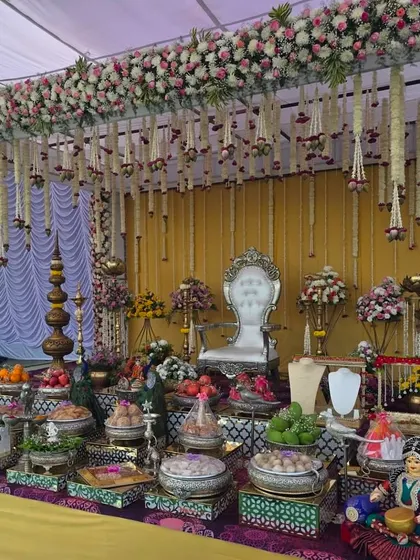 An elegant outdoor Seemantham ceremony with a floral canopy. The stage features a silver throne and a beautiful arrangement of traditional offerings, creating a serene and picturesque setting.