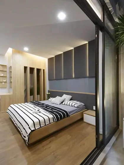 A modern bedroom design that connects seamlessly with an outdoor space. The wood flooring and paneled headboard create a warm and natural feel, while the glass sliding door invites the outdoors in.