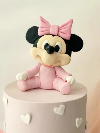 A close-up of the handcrafted baby Minnie Mouse figure from the two-tiered cake. Every detail, from her bow to her expression, is sculpted from fondant.