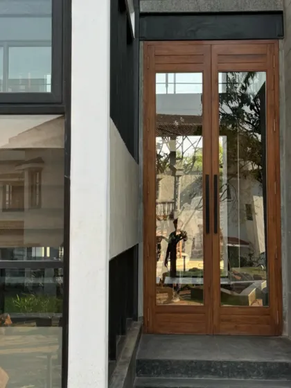 The entrance of the 6AM House, featuring simple, elegant wooden doors that contrast with the raw, modern structure. The reflection in the glass captures the surrounding environment, integrating it into the facade.