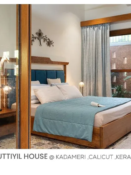 This bedroom in Kuttiyil House features a blue upholstered headboard and a large window that provides ample light and a view of the jali-walled courtyard.