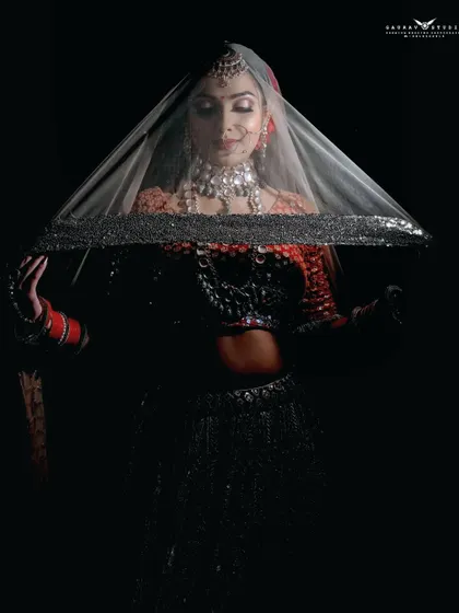 A dramatic shot using a veil against a black background. The lighting creates a mysterious and alluring silhouette, focusing on the bride's form and the sparkling veil.
