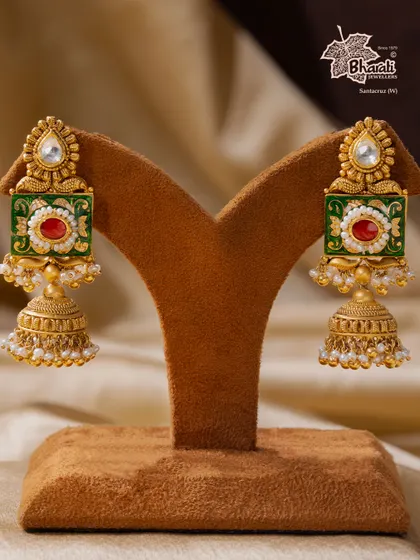 A tribute to India’s timeless artistry. These Meenakari jhumka earrings are hand-enameled with vibrant green and red floral motifs, framed in antique gold. The design is completed with a classic bell shape and delicate pearls, making them a regal addition to any ensemble.