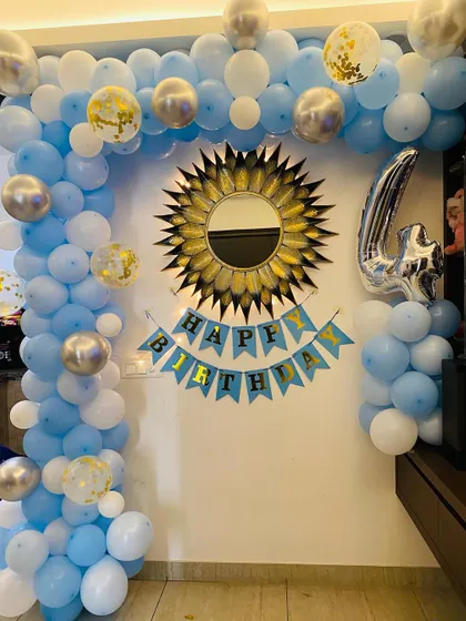 A 4th birthday party setup at home with a blue, white, and silver balloon arch.