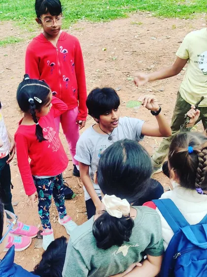 An older child shares his knowledge about a leaf he has found, teaching the younger children in a beautiful moment of peer-to-peer learning during our park visit.