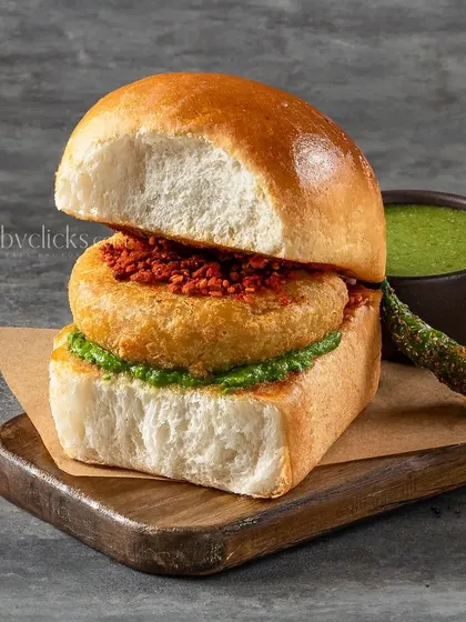A cross-section of a Vada Pav, showing the layers of potato vada, chutneys, and soft pav.
