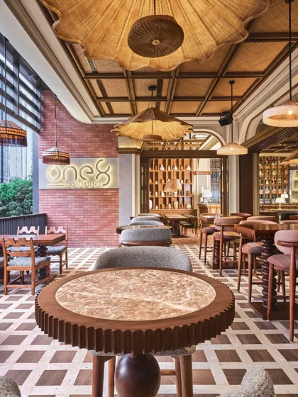The checkerboard flooring at One 8 Commune, made from wood and polished stone, is a centerpiece of the design. It grounds the space with a timeless pattern while complementing the warm, natural textures of the rattan lighting and marble-topped tables.