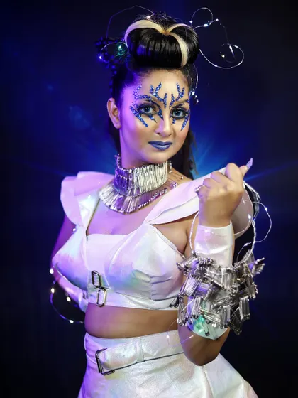 An ethereal, alien-like character with blue crystal makeup and a futuristic white outfit. I teach you how to use embellishments and lighting to create magical effects.